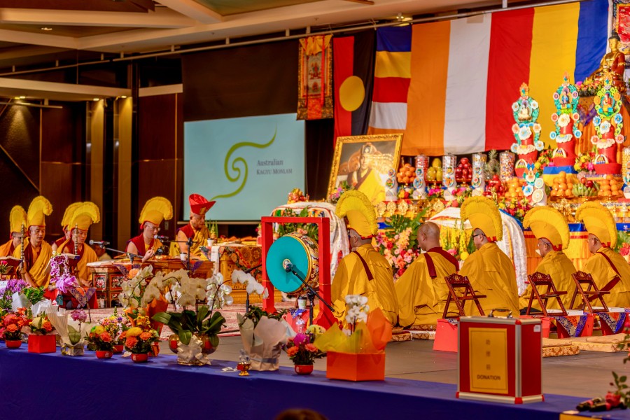 several Buddhist monastics sitting on a stage in prayer