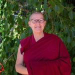 Venerable Yeshe standing in front of hedge plants, dressed in monastic robes.