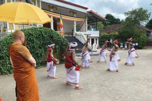 Buddhist monk watching a performance of drummers and dancers.